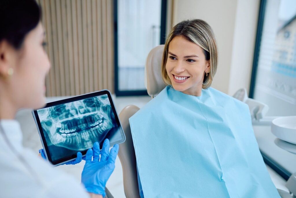 Smiling dental patient reviewing a dental X-ray on a tablet with her dentist